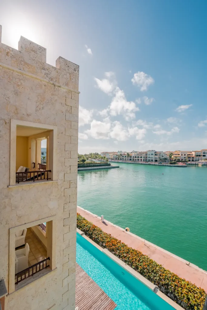 Turquoise lagoon, sandy beach, and waterfront buildings viewed from balcony with pool below.