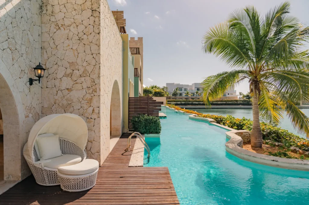 Pool deck with white pod chair, wooden decking, palm tree, and waterfront views.