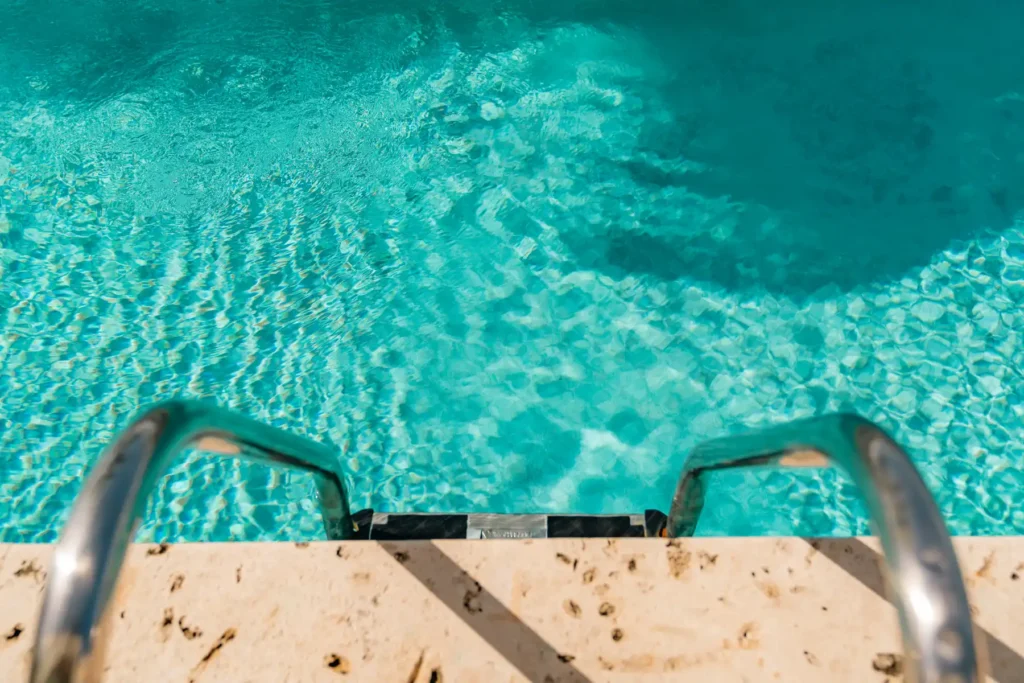 Clear turquoise swimming pool water viewed from pool ladder edge.